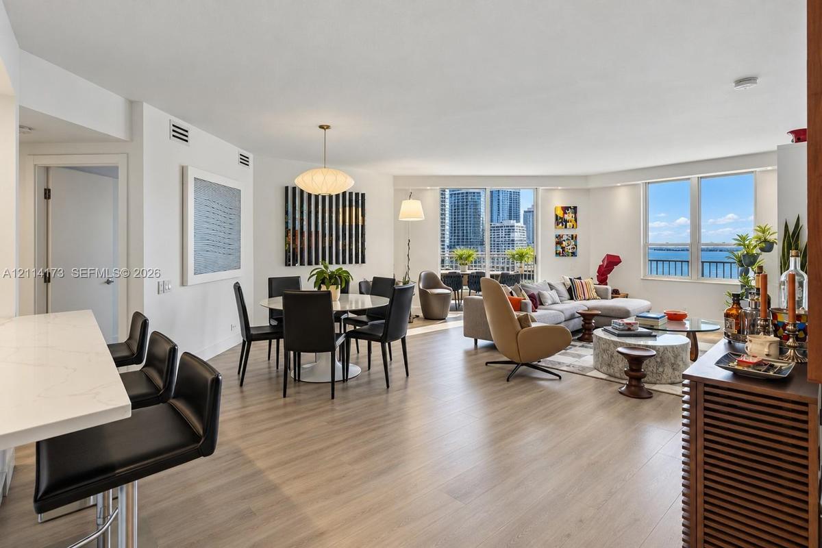Open-concept main living area featuring light wood-finish flooring, quartz-surfaced kitchen island, recessed lighting, and expansive floor-to-ceiling 
