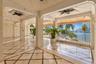Covered terrace featuring stone tile flooring with decorative inlay, structural columns, ceiling-mounted fans, and metal railings overlooking the wate