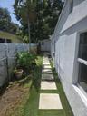 Side yard featuring a concrete paver walkway, artificial turf landscaping, white vinyl privacy fencing, and a detached storage structure