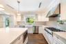 Kitchen featuring white cabinetry, quartz countertops, a farmhouse-style apron sink, professional-grade stainless steel range with matching hood, and 