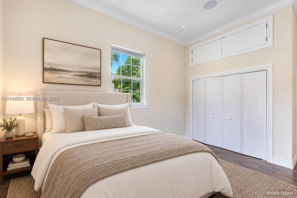 Neutral-toned room featuring dark wood-finish flooring, white bi-fold closet doors, additional overhead storage cabinetry, and a window with exterior 
