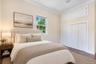 Neutral-toned room featuring dark wood-finish flooring, white bi-fold closet doors, additional overhead storage cabinetry, and a window with exterior 
