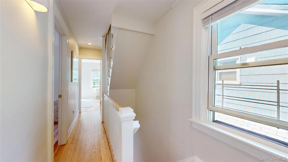 Hallway featuring wood-finish flooring, white painted walls, and a staircase with a white wood railing