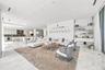 Open-concept interior featuring light-toned stone flooring, recessed ceiling lighting, and a wall-mounted shelving unit with integrated cabinetry