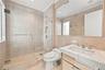 Full-wall stone tiling, glass-enclosed walk-in shower with built-in recessed niche, vanity with integrated basin, polished stone countertop, and large