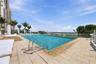 Rectangular swimming pool featuring a stone-tile deck, metal entry ladders, glass perimeter fencing, and an ocean horizon