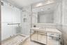 Full-height stone wall surfacing, frameless glass shower enclosure, vanity with integrated sink, mirrored cabinet base, and wall-to-wall vanity mirror