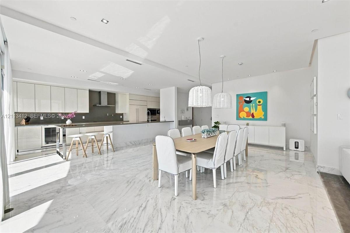 Open-concept kitchen and dining area featuring stone-finish flooring, high-gloss cabinetry, stainless steel range hood, built-in refrigerator, and dua