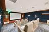 Media room featuring tiered flooring, dark blue upholstered wall panels, integrated wood-finish wall accents, recessed lighting, and a built-in projec