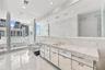Full-length stone vanity with dual undermount sinks, expansive wall-to-wall mirror, floor-to-ceiling natural stone wall and floor tile, glass-enclosed