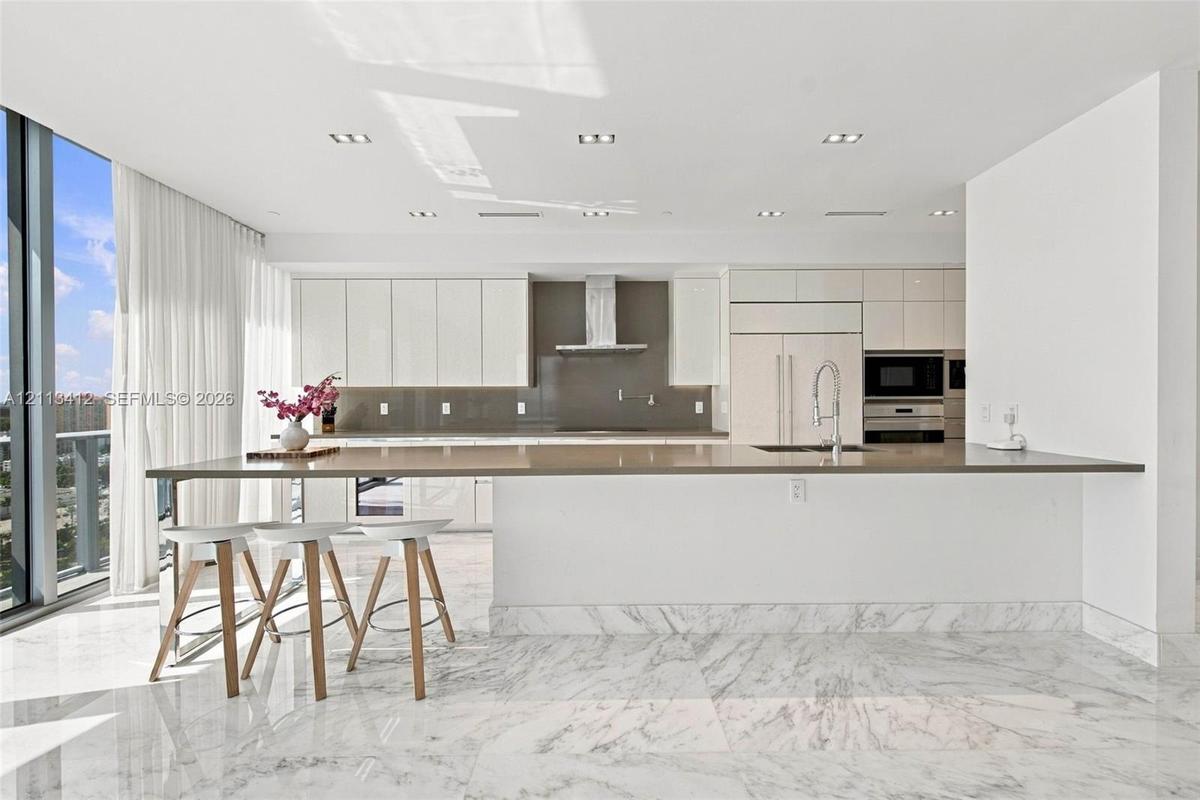 Gourmet kitchen featuring high-gloss cabinetry, stone-surface breakfast bar, built-in stainless steel appliances, recessed ceiling lighting, and polis