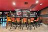 Curved wet bar featuring a stone-faced front, integrated shelving, mirror back-splash, overhead stemware rack, and recessed lighting