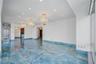 Open interior featuring polished blue stone flooring, recessed ceiling lighting, three ornate crystal chandeliers, and floor-to-ceiling glass panel do