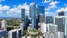 High-rise glass facade skyscraper featuring an elevated pool deck with lush landscaping, centered within a dense urban skyline