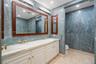 Double vanity with white cabinetry, stone-finish countertops, brass-toned fixtures, wood-framed mirrors, and floor-to-ceiling stone wall cladding