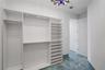 Custom built-in white shelving and cabinetry, multi-level hanging rods, polished blue-toned stone-finish tile flooring, and multi-arm chandelier