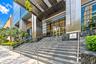 Grand entryway featuring a polished stone staircase, dual metal railings, glass-paneled doors, and a suspended metallic awning