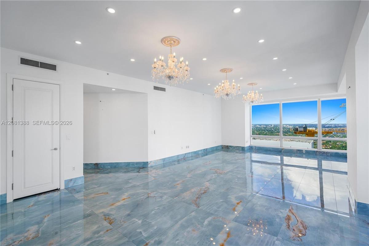 Polished stone flooring with blue-toned veining, three tiered crystal chandeliers with ceiling medallions, recessed lighting, and floor-to-ceiling win