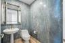Full-height wall tiling with a natural stone-finish pattern, pedestal sink, gold-tone faucet, and gold-trimmed rectangular mirror