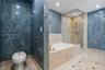 Bathroom featuring floor-to-ceiling blue veined stone wall tiling, a built-in soaking tub with beige stone surround, a glass-enclosed shower with meta