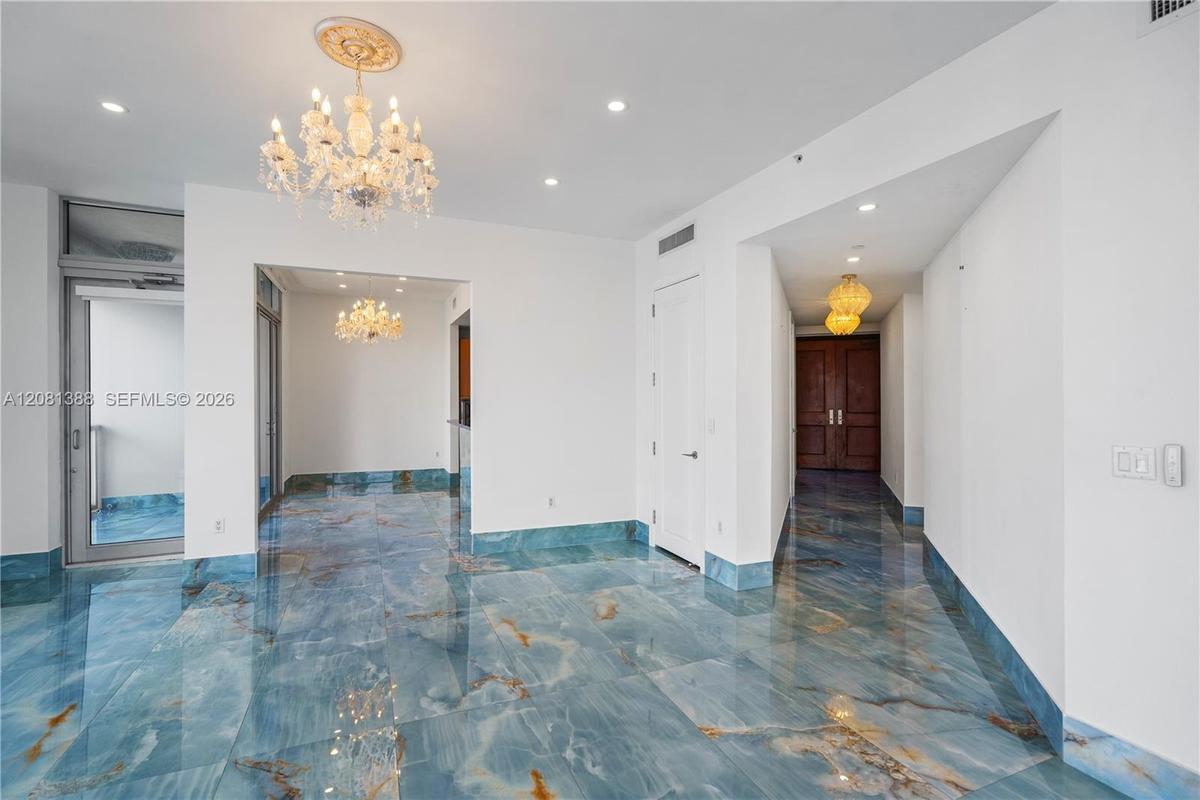 Polished blue stone flooring with gold veining, ornate crystal chandelier, decorative ceiling medallion, recessed lighting, and solid wood double-entr