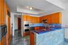 Kitchen featuring natural stone countertops and tile flooring, wood-finish cabinetry, stainless steel double wall ovens, and a recessed ceiling tray