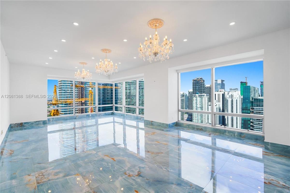 Polished blue-toned stone flooring, floor-to-ceiling windows, crystal chandeliers, recessed lighting, and ornate ceiling medallions