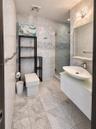 Full-height natural stone tiling, floating vanity with an oval vessel sink, frameless glass-enclosed shower, wall-mounted light fixture, and polished 
