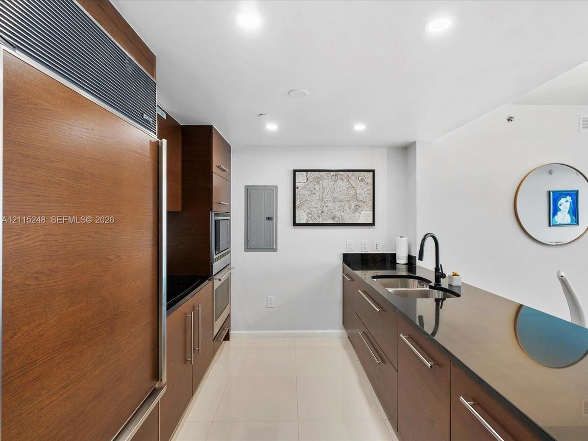 Kitchen featuring wood-finish cabinetry, built-in stainless steel appliances, dark stone countertops, undermount sink with a matte black faucet, and r