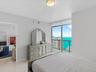 Floor-to-ceiling windows, porcelain tile flooring, neutral wall palette, flush-mount lighting, and private balcony with coastal and cityscape scenery