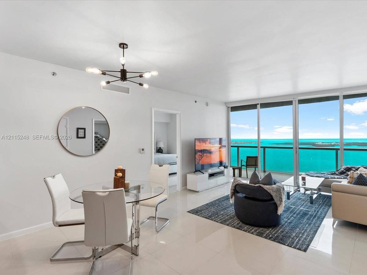 Open-concept space featuring floor-to-ceiling glass paneling, polished tile flooring, a geometric multi-arm pendant light fixture, and a glass-railed 