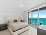 Floor-to-ceiling glass sliding doors, private balcony with metal railing, neutral tile flooring, flush-mount circular lighting fixture, and panoramic 