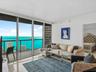 Floor-to-ceiling sliding glass panels, balcony with metal railing, polished neutral-toned flooring, and expansive water scenery