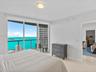 Floor-to-ceiling sliding glass doors, water backdrop, covered balcony with metal railing, and tile flooring