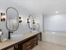 Dual vanity featuring stone-surfaced countertops, vessel sinks with matte black faucets, wood-finish cabinetry, and oval mirrors with integrated wall-