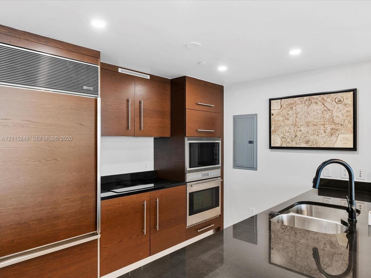 Kitchen featuring dark wood-finish cabinetry, built-in stainless steel double wall ovens, panel-ready refrigerator, polished stone countertops, and a 