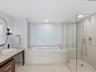 Bathroom featuring a stone-tile surround soaking tub, a frameless glass-enclosed shower with handheld fixture, stone-tile flooring, and a floating van