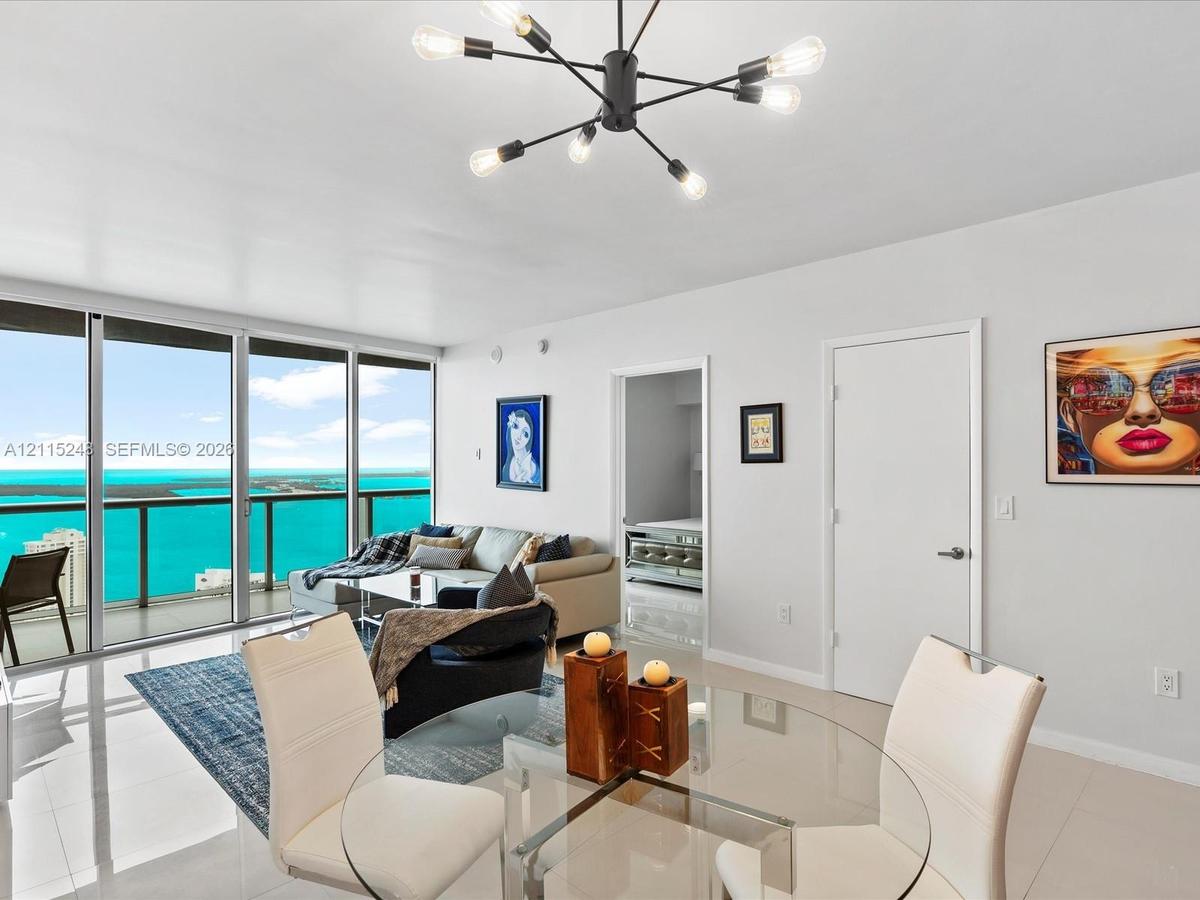 Floor-to-ceiling sliding glass doors, water backdrop, large-format tile flooring, multi-arm sputnik-style chandelier, and recessed lighting