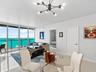 Floor-to-ceiling sliding glass doors, water backdrop, large-format tile flooring, multi-arm sputnik-style chandelier, and recessed lighting