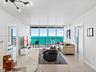 Living area featuring floor-to-ceiling glass sliding doors, a glass-railed balcony, large-format tile flooring, and multi-arm chandelier lighting