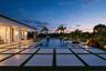 Spacious outdoor patio with large format pavers and synthetic turf inlays, featuring a rectangular swimming pool, integrated landscaping, and a covere