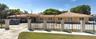 Single-story exterior featuring a clay tile roof, stucco finish, gated paved entrance, and masonry pillars