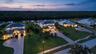 Aerial perspective of waterfront properties featuring multi-story residences, paved driveways, hipped rooflines, and manicured lawns