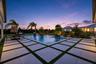 Rectangular swimming pool featuring a grid-patterned paver deck with integrated turf detailing, manicured landscaping, and mature palm trees