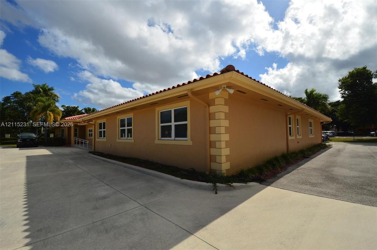Stucco exterior featuring quoined corners, a clay tile roof, and a paved parking area