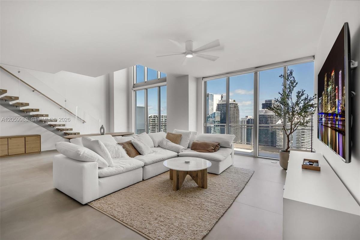 Open-concept living space featuring floor-to-ceiling windows, porcelain tile flooring, a floating staircase with glass railing, and a central ceiling 