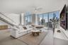 Open-concept living space featuring floor-to-ceiling windows, porcelain tile flooring, a floating staircase with glass railing, and a central ceiling 