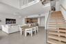 Open-concept interior featuring wood-tread staircase with glass railing, large-format neutral flooring, double-height ceiling, built-in cabinetry, and