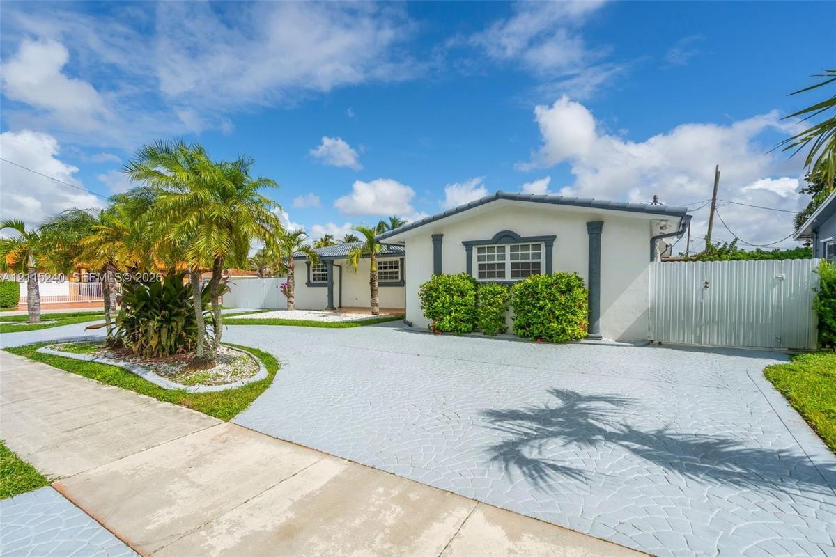 Single-story exterior featuring light-toned stucco walls, contrasting window trim, decorative columns, textured concrete driveway, and white privacy f