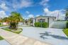 Single-story exterior featuring light-toned stucco walls, contrasting window trim, decorative columns, textured concrete driveway, and white privacy f